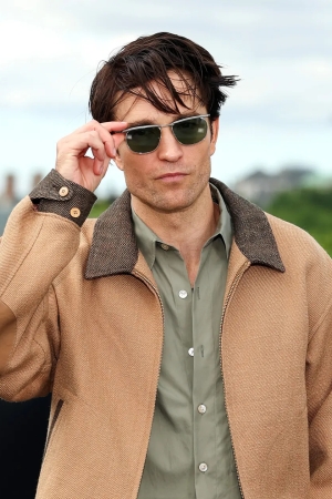 Robert Pattinson, gri keten-yün karışımlı Visvim Strato ceket, siyah tişört ve siyah pantolon ile bir galada poz veriyor