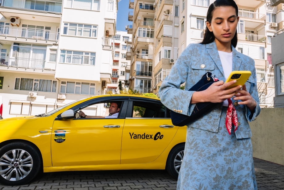 İstanbul'da Yandex Go taksisinin yanında akıllı telefonundan yolculuğunu planlayan bir kullanıcı.