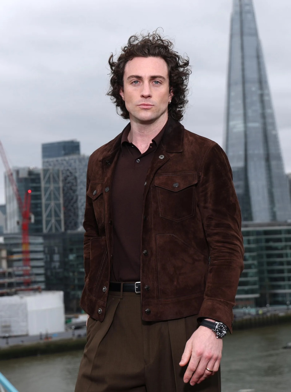 Aaron Taylor-Johnson'ın doğal kıvırcık uzun saç modeliyle objektife poz verdiği görünüm.