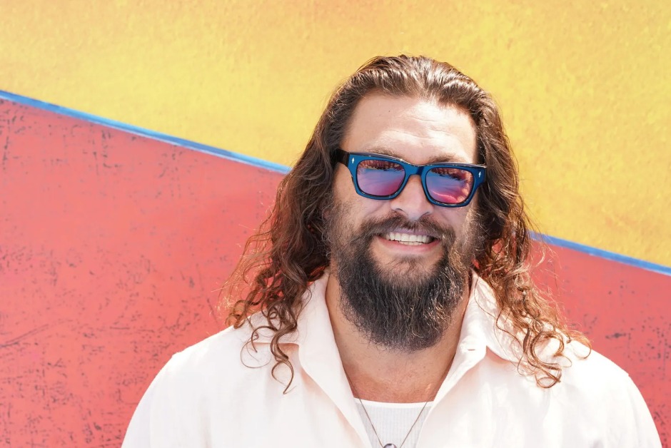 Jason Momoa'nın omuz hizasındaki uzun dalgalı saç modeli ve sakalıyla verdiği poz.