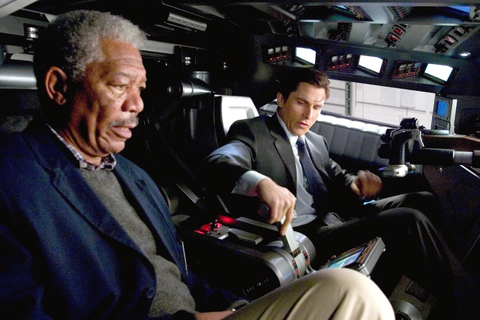 Christopher Nolan'ın Batman Begins (2005) filminden bir sahne; Lucius Fox ve Bruce Wayne, Batmobile'ın kokpitinde aracı inceliyor.
