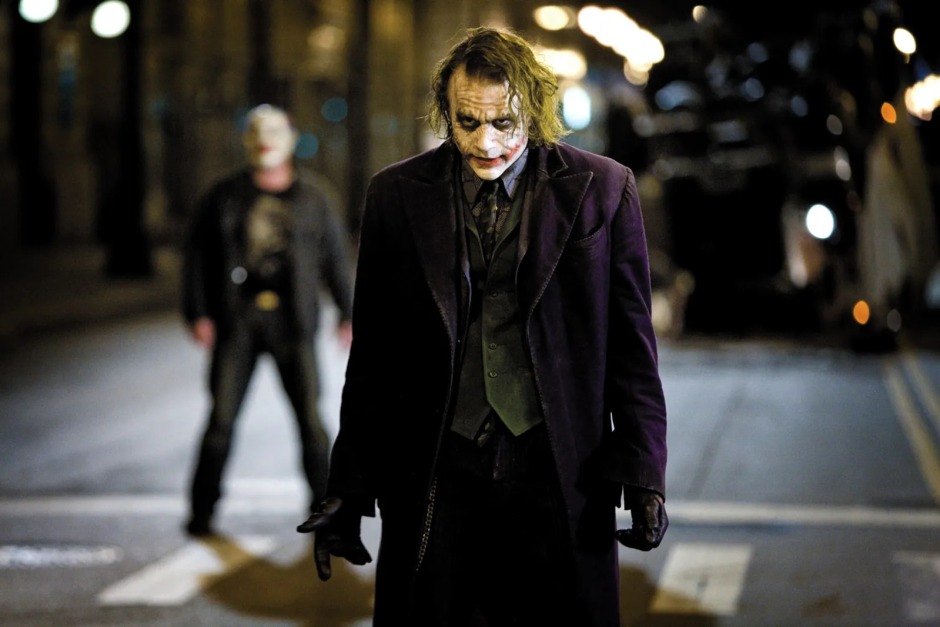 Christopher Nolan'ın The Dark Knight (2008) filminden bir sahne; Heath Ledger'ın canlandırdığı Joker, gece vakti Gotham sokaklarında ilerlerken arka planda Batman görülüyor.