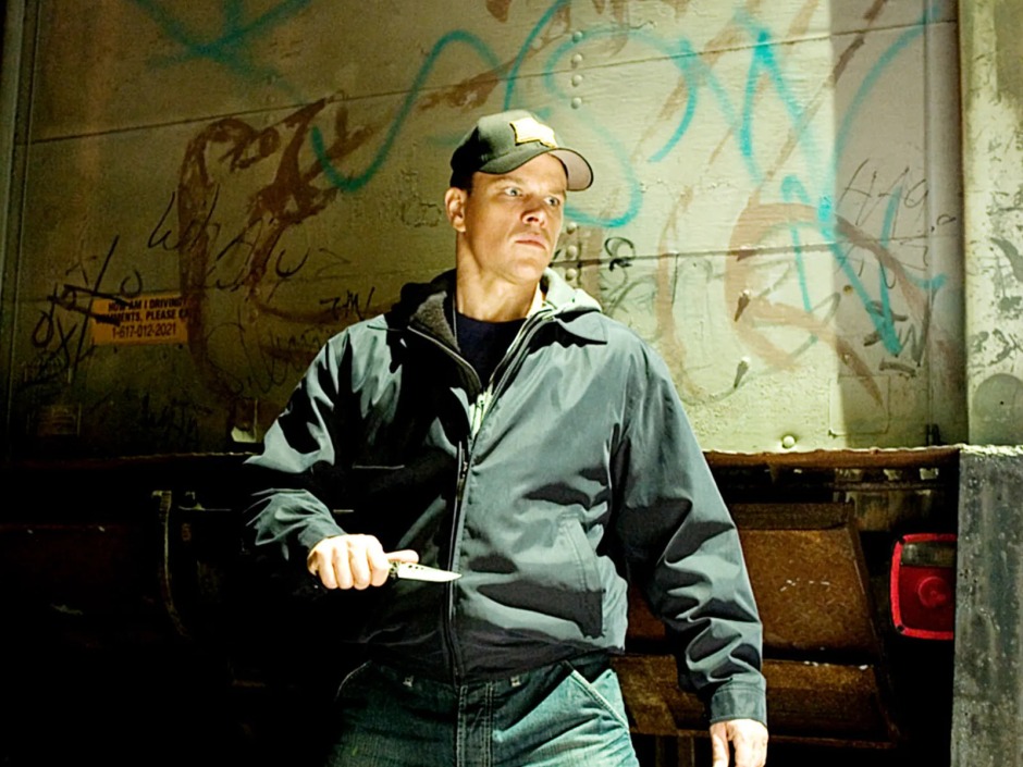 Martin Scorsese'nin The Departed (2006) filminden bir sahne; Matt Damon'ın canlandırdığı Colin Sullivan, elinde silahla karanlık bir sokakta ilerliyor.