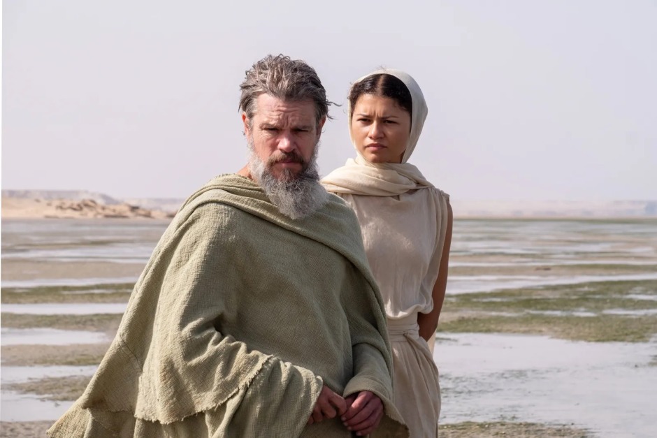 Christopher Nolan'ın The Odyssey (2026) filminden bir sahne; Matt Damon ve Zendaya antik dönem kıyafetleriyle kıyıda yan yana duruyor.