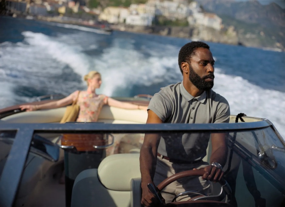 Christopher Nolan'ın Tenet (2020) filminden bir sahne; John David Washington sürat teknesini kullanırken, arka planda Elizabeth Debicki'nin canlandırdığı karakter denize doğru bakıyor.