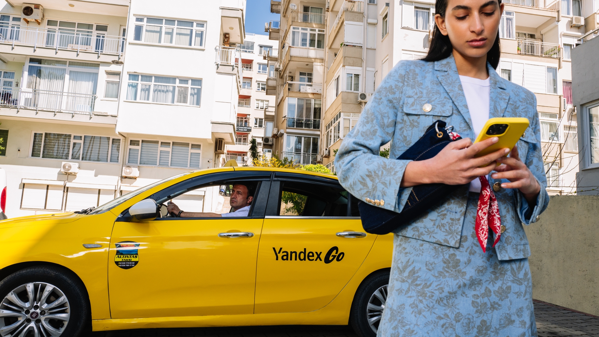 İstanbul'da Yandex Go taksisinin yanında akıllı telefonundan yolculuğunu planlayan bir kullanıcı.